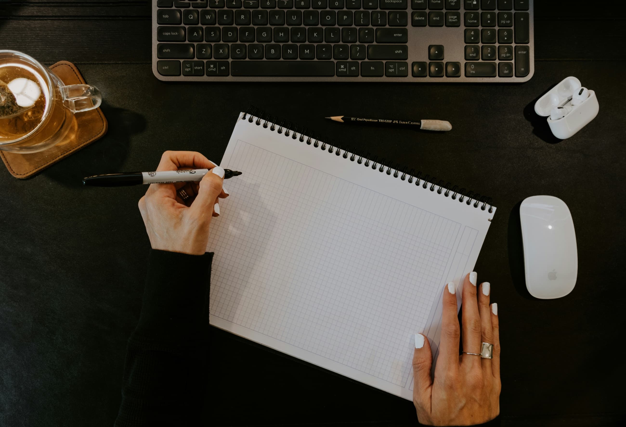A hand about to write on a blank grid-paper pad on a dark desk.