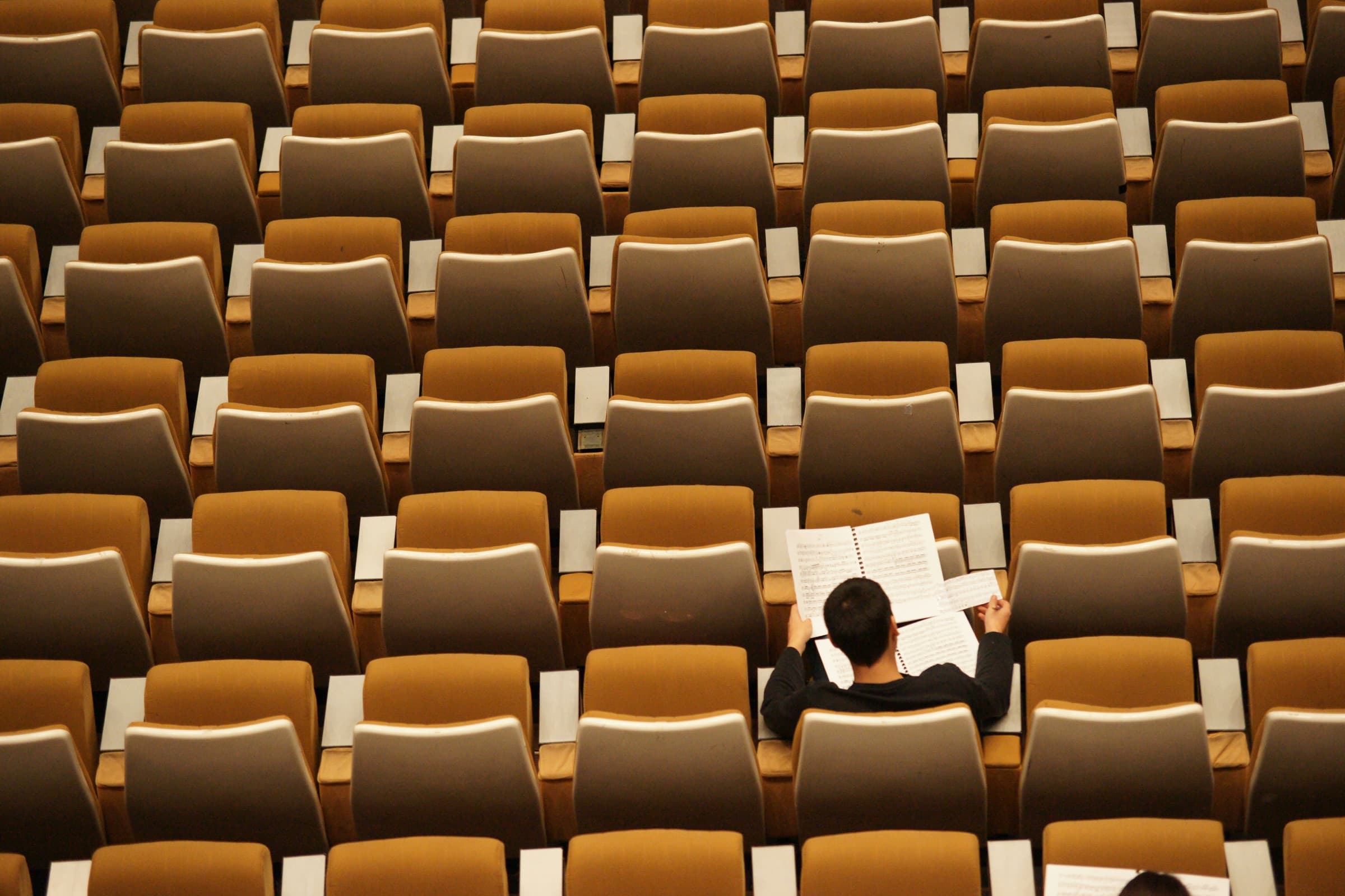 One student sitting alone reading in an otherwise empty lecture hall.